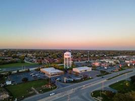 vista aérea da área urbana com torre de água proeminente na ampla rodovia da cidade grande área industrial com estacionamento Casas unifamiliares com o sol começando a se pôr foto