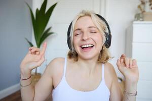 dançando menina escuta para música, mulher desgasta sem fio fones de ouvido e goza som qualidade, canta foto