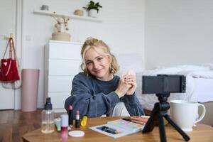 retrato do lindo loiro mulher, menina mostra cora, beleza produtos, gravação em digital Câmera, criando conteúdo para social meios de comunicação conta, vlogger recomendando Itens dentro vlog foto