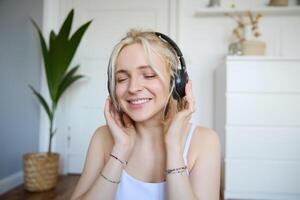 conceito do pessoas e estilo de vida, fechar acima do lindo loiro mulher dentro sem fio fones de ouvido, escuta para música, goza Boa qualidade som dentro Novo fones de ouvido foto