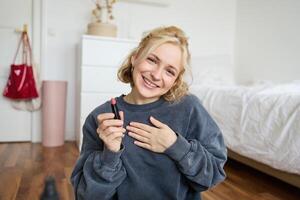 retrato do bonitinho, carismático beleza blogueiro, mulher senta dentro uma quarto com batom dentro mão, falando sobre inventar, conversando com seguidores, gravação conectados corrente em social meios de comunicação aplicativo foto