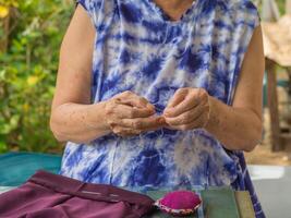 fechar-se do mãos Senior mulher tentando para fio uma agulha para de costura pano. espaço para texto. conceito do envelhecido pessoas e relaxamento foto