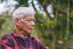 retrato do idosos homem braços cruzado e olhando longe enquanto em pé dentro uma jardim foto