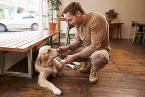 retrato do bonito homem jogando com dele cachorro dentro uma cafeteria, uma cara detém dele animal pata dentro mão e sorrisos, gasta Tempo dentro animal amigáveis espaço foto