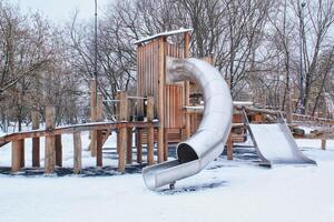 de madeira Parque infantil fez do natural ecológico material dentro público cidade parque com neve às inverno tempo. moderno segurança crianças ao ar livre equipamento. inverno Atividades. crianças descansar e jogos em aberto ar foto