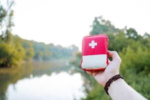 uma pequeno vermelho saco com uma branco cruzar, uma homem segurando uma primeiro ajuda kit dentro dele mão, uma rastrear para Socorro com prejuízo uma saco com medicação primeiro ajuda kit. foto