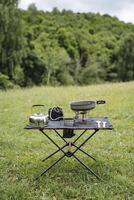 turista utensílios ficar de pé em uma mesa fez do tecido, uma compactar conjunto do turista equipamento, uma acampamento cozinha, uma gás queimador, uma chaleira com uma caneca, minimalismo. foto