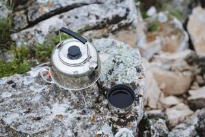 beber chá dentro natureza dentro a montanhas, uma lata chaleira carrinhos em uma pedra chá derramado para dentro uma caneca, café da manhã dentro a montanhas, ferver água, preparar uma quente bebida, almoço em uma caminhada. foto