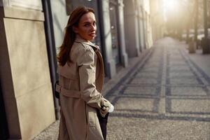 atraente mulher dentro casaco cruzando a cidade rua e olhando às Câmera. borrado fundo foto