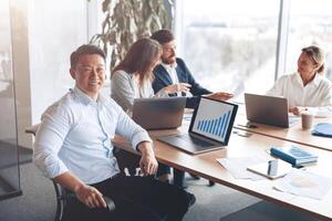 retrato do sorridente ásia homem de negocios trabalhando em uma computador portátil durante uma encontro com uma equipe foto