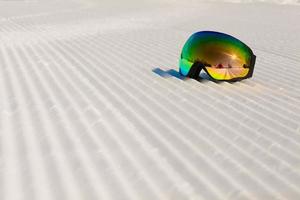 óculos de esqui em uma neve limpa e em uma pista de esqui vazia foto