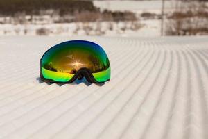 óculos de esqui em uma neve limpa e em uma pista de esqui vazia foto