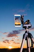 smartphone no tripé capturando imagem do pôr do sol no modo vertical foto