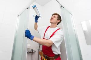 jovem homem reparação porta do chuveiro cabine dentro banheiro. foto