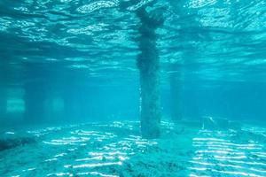 vista subaquática sob um píer com pilares e luz solar foto