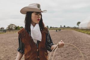 bonita chinês vaqueira jogando a laço dentro uma cavalo Pomar, pasto foto