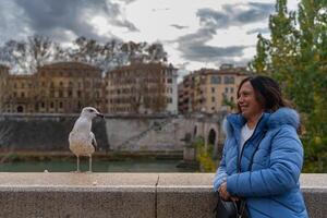 meio envelhecido fêmea turista fotografando com dela Móvel telefone uma gaivota em uma ponte dentro Roma foto