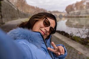feliz meio envelhecido mulher em período de férias levando uma selfie em a bancos do a Tibre rio dentro Roma foto