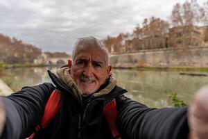 feliz meio envelhecido homem em período de férias levando uma selfie em a bancos do a Tibre rio dentro Roma foto