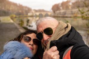 feliz meio envelhecido casal em período de férias levando uma selfie em a bancos do a Tibre dentro Roma foto