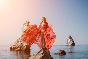 mulher viagem mar. jovem feliz mulher dentro uma grandes vermelho vestir posando em uma de praia perto a mar em fundo do vulcânico rochas, gostar dentro Islândia, partilha viagem aventura viagem foto