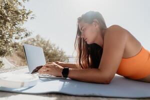 mulher computador portátil mar. trabalhando remotamente em Beira Mar. feliz bem sucedido mulher fêmea trabalhador autonomo trabalhando em computador portátil de a mar às pôr do sol, faz uma o negócio transação on-line. freelance, controlo remoto trabalhos em período de férias foto