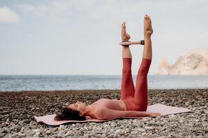 mulher mar pilates. desportivo feliz meio envelhecido mulher praticando ginástica em de praia perto mar, sorridente ativo fêmea Treinamento com anel em ioga esteira fora, desfrutando saudável estilo de vida, harmonia e meditação foto