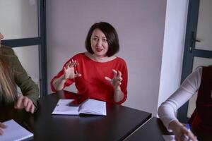 uma mulher dentro uma vermelho suéter gestos emocionalmente às uma encontro dentro a escritório foto