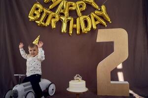 uma criança pequena é feliz com uma aniversário bolo e apresenta em dele segundo aniversário foto