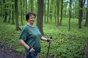 idosos mulher é acionado dentro nórdico caminhando com Gravetos dentro a Primavera floresta foto