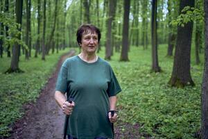 idosos mulher é acionado dentro nórdico caminhando com Gravetos dentro a Primavera floresta foto