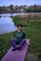 a velho mulher meditando dentro a manhã em a banco do a rio, veio a partir de casa de bicicleta foto