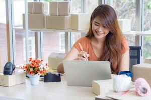 empresária vestindo casual pano sentado dentro a escritório. a trabalhos escrivaninha dentro a escritório tem uma computador portátil, código de barras leitor preparar para ordens a partir de clientes. conceito do o negócio e comércio eletrônico foto