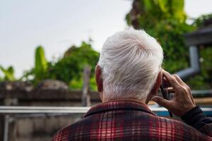 costas Visão do idosos homem usando Smartphone dentro dele jardim foto