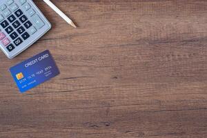 topo Visão do uma azul crédito cartão, lápis, e calculadora em uma de madeira mesa. espaço para texto. madeira textura fundo. o negócio e finança conceito foto