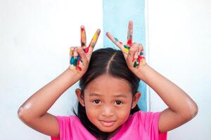 fofa pequeno menina com colorida pintado mãos em parede fundo foto