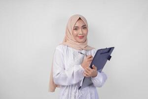 sorridente jovem ásia muçulmano mulher vestindo branco vestir e hijab segurando uma documento, isolado de branco fundo. Ramadã e eid Mubarak conceito foto