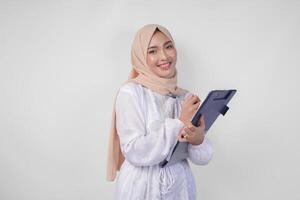 sorridente jovem ásia muçulmano mulher vestindo branco vestir e hijab segurando uma documento, isolado de branco fundo. Ramadã e eid Mubarak conceito foto