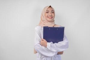 sorridente jovem ásia muçulmano mulher vestindo branco vestir e hijab segurando uma documento, isolado de branco fundo. Ramadã e eid Mubarak conceito foto