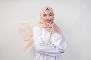 elegante jovem ásia muçulmano mulher vestindo branco vestir com hijab acenando dentro a vento, modelagem pose em branco fundo foto