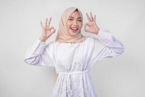 retrato do ásia muçulmano mulher dentro branco vestir e hijab fazer a OK, bom, agradável placa gesto usando dedos. Ramadã e eid Mubarak conceito foto