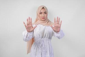 jovem ásia muçulmano mulher vestindo branco vestir e hijab mostrando dela Palma para faço uma Pare gesto com sério expressão foto