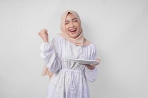 alegre jovem ásia muçulmano mulher dentro hijab fazendo uma bem sucedido ganhar gesto com cerrado punho enquanto apresentando a esvaziar prato e cópia de espaço sobre isto foto