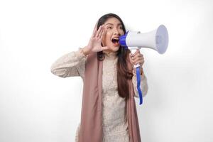 animado jovem ásia muçulmano mulher vestindo lenço de cabeça véu hijab gritando às megafone, isolado em branco fundo estúdio. Ramadã e eid Mubarak conceito. foto