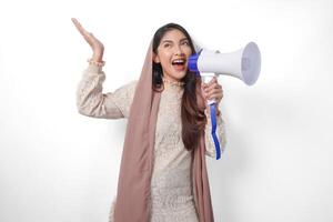 jovem ásia muçulmano mulher vestindo lenço de cabeça véu hijab gritando às megafone enquanto apontando acima para a cópia de espaço para cima, isolado em branco fundo estúdio. Ramadã e eid Mubarak conceito. foto