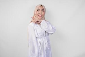 alegre ásia mulher vestindo hijab e branco vestir apontando para a cópia de espaço atrás, em pé sobre isolado branco fundo. Ramadã e eid Mubarak propaganda conceito foto