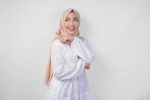 alegre ásia mulher vestindo hijab e branco vestir apontando para a cópia de espaço atrás, em pé sobre isolado branco fundo. Ramadã e eid Mubarak propaganda conceito foto