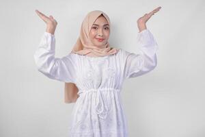 feliz ásia mulher vestindo hijab e branco vestir apontando acima para a cópia de espaço acima, em pé sobre isolado branco fundo. Ramadã e eid Mubarak propaganda conceito foto