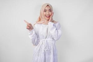 animado ásia mulher vestindo hijab e branco vestir apontando para a cópia de espaço em dela certo lado, em pé sobre isolado branco fundo. Ramadã e eid Mubarak propaganda conceito foto