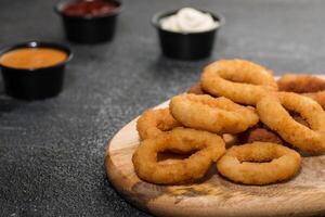 crocante cebola argolas com mergulho molho e maionese isolado em de madeira borda com mergulho molho topo Visão do grade Comida em Sombrio cinzento fundo foto